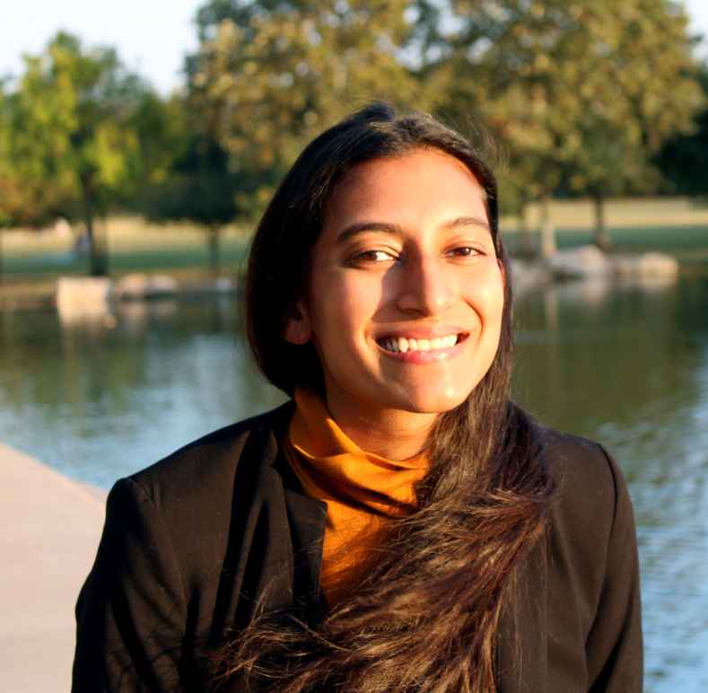 Photo: Savannah Kumar poses for a photo outdoors. She stands in front of a body of water with trees in the background.