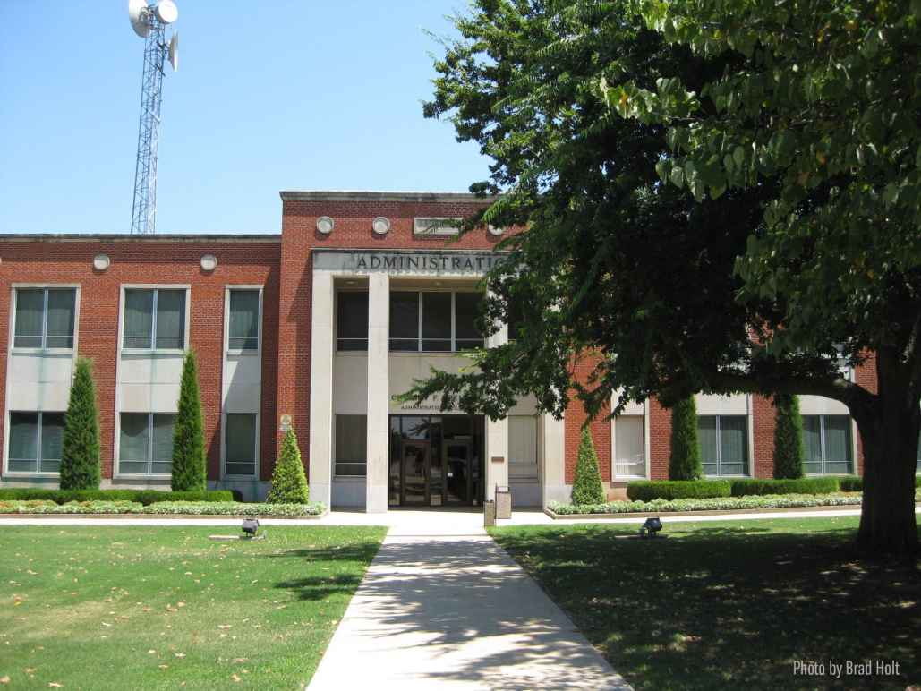 Photo: A tree in the foreground obscures a portion of a brick administration building in the background 