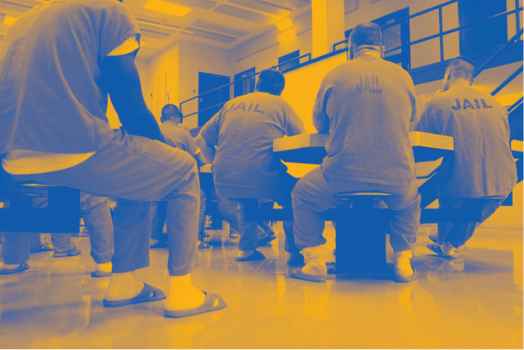 Image: A stylized photo shows men wearing uniforms that say "Jail" on their backs. They sit around tables in a carceral facility