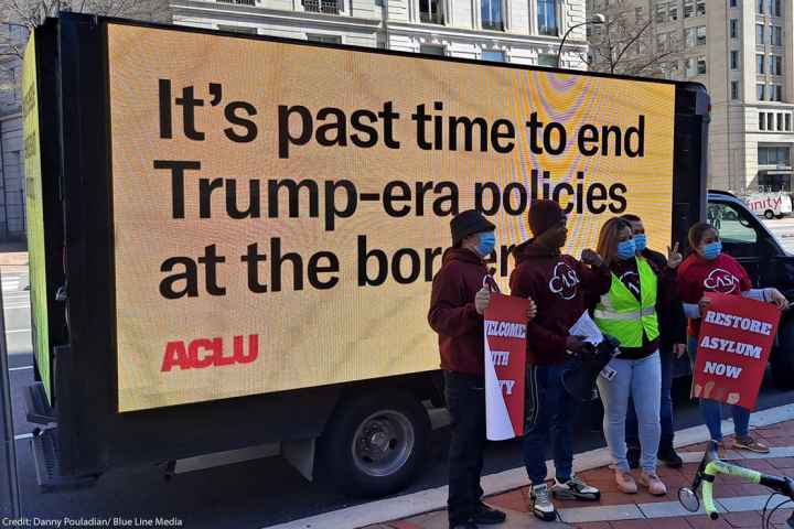 Demonstrators standing in front of a mobile billboard that says, “It’s past time to end Trump-era policies at the border.”