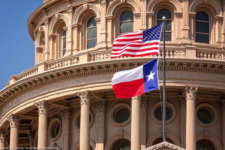American and Texas state flags flying on the dome of the Texas State Capitol building.