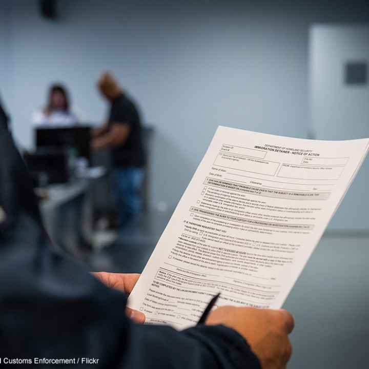 An ICE agent holding an Immigration Detainer form.