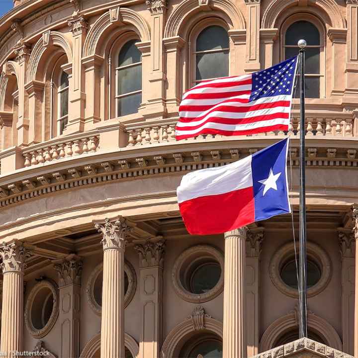 American and Texas state flags flying on the dome of the Texas State Capitol building.