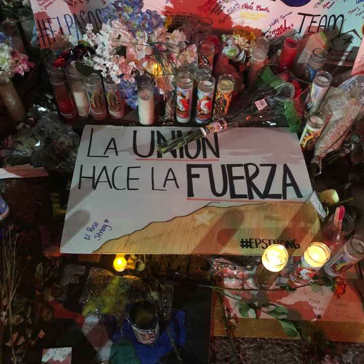 El Paso Strong Photo: Handwritten signs, candles, and flowers adorn a section of a street. Pictured at center is a sign that says "La union hace la fuerza."