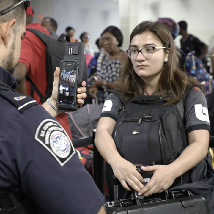 CBP agent scanning the face of a young woman using his smart phone