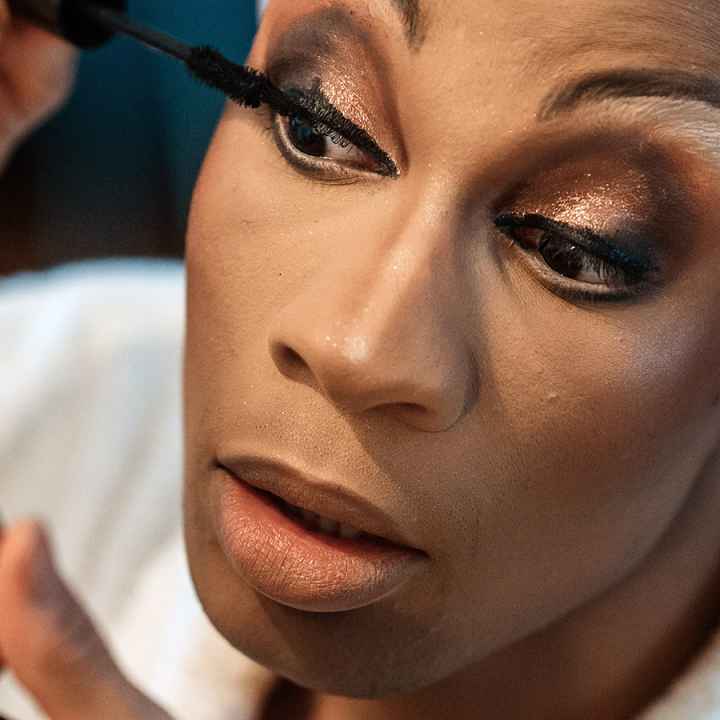 A drag performer applies mascara
