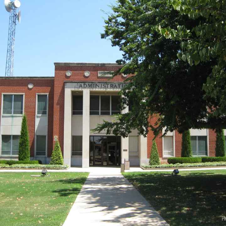 School District Photo: A tree in the foreground obscures a portion of a brick administration building in the background
