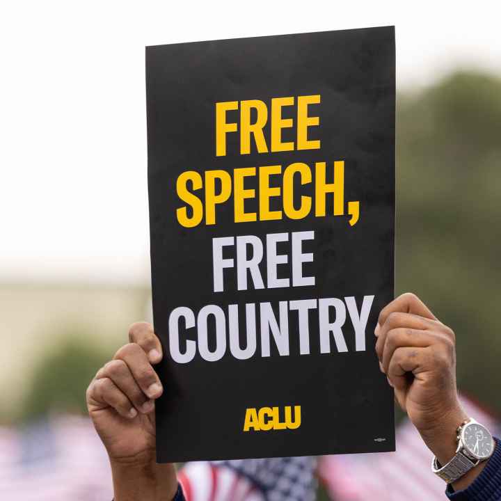 A demonstrator (with only their hands visible) holds up a sign that reads " FREE SPEECH, FREE COUNTRY - ACLU".