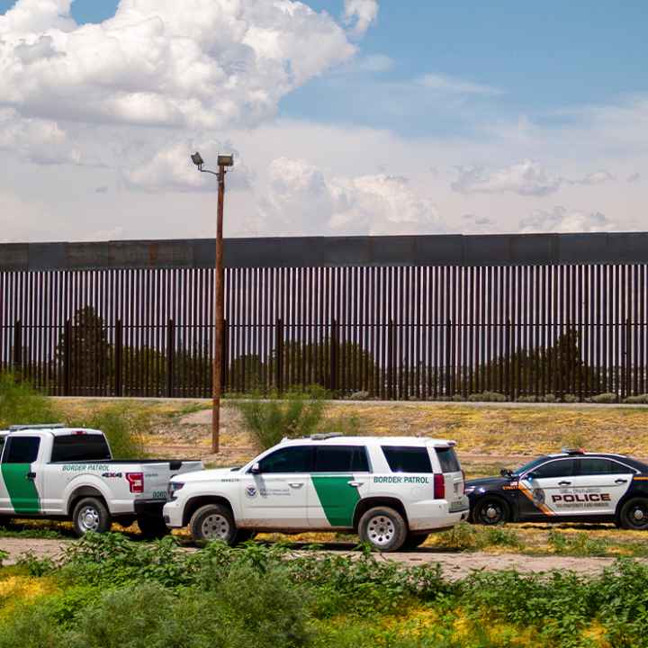 U.S. Border patrol vehicles converge with local police car by border fence.