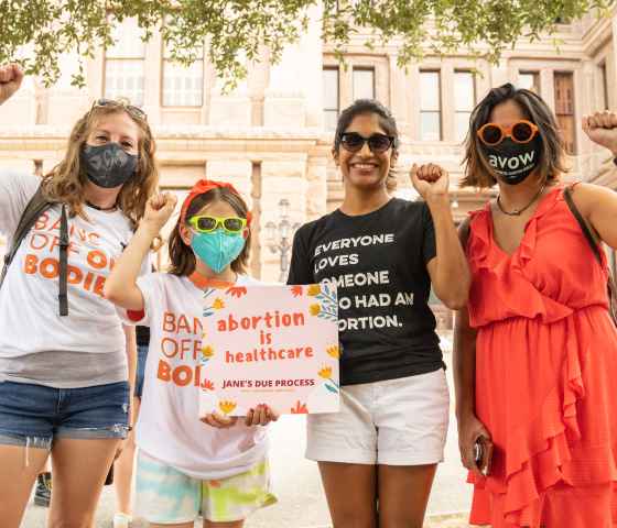 an image of four people with their fists up holding a sign that says abortion is healthcare